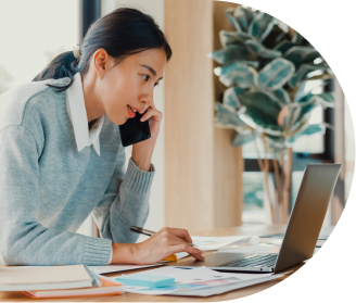 Mulher se concentra no computador e conversa ao telefone com colega